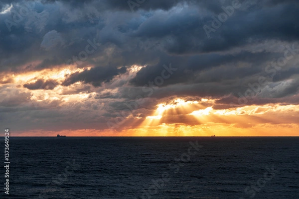 Obraz Gelendzhik resort. The sky is cloudy and the sun is setting. The sun is shining through the clouds, creating a beautiful orange and pink sky. The ocean is calm and the horizon is visible
