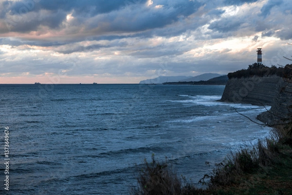 Obraz Gelendzhik resort. A lighthouse is visible on the shoreline of a body of water. The sky is cloudy and the water is calm