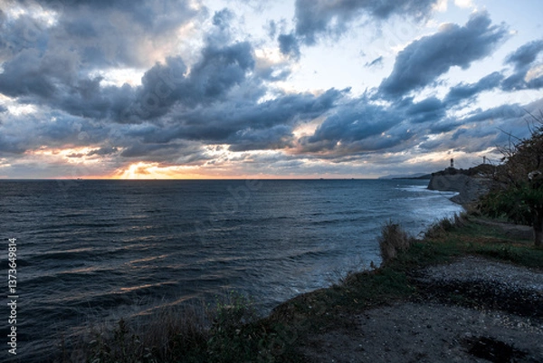 Obraz The sky is cloudy and the sun is setting. The ocean is calm and the water is dark blue
