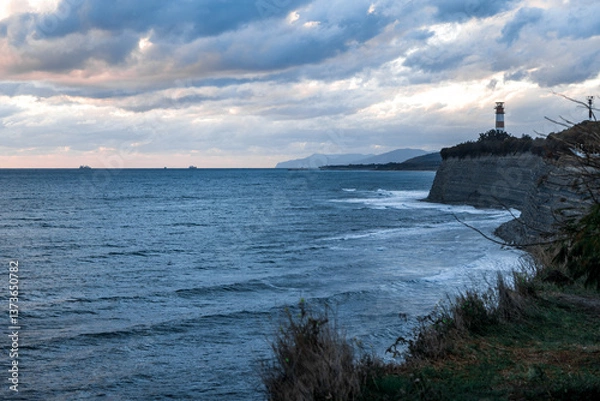Obraz Gelendzhik resort. A lighthouse is visible on the shoreline of a body of water. The sky is cloudy and the water is calm