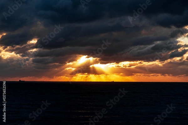 Obraz Gelendzhik resort. The sky is cloudy and the sun is setting. The sun is shining through the clouds, creating a beautiful orange and pink sky. The ocean is calm and the horizon is visible