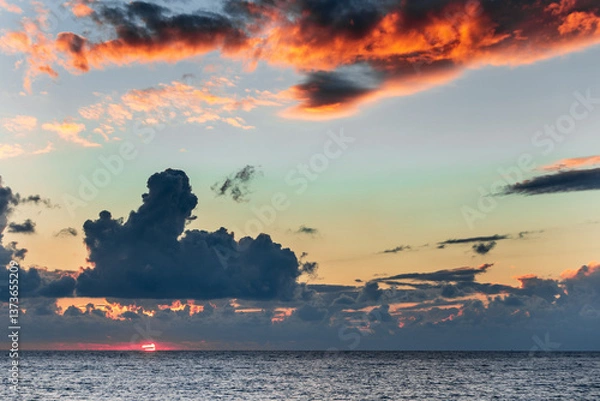 Obraz A beautiful sunset over the ocean with a large cloud in the sky. The sky is a mix of orange and blue colors