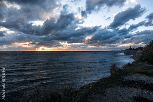 Obraz The sky is cloudy and the sun is setting. The ocean is calm and the water is dark blue