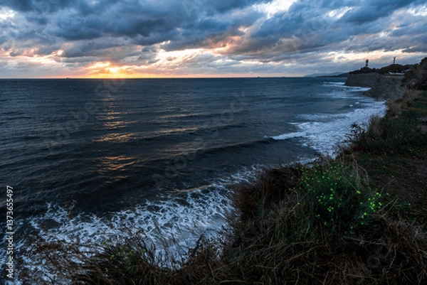 Obraz The sky is cloudy and the sun is setting. The ocean is calm and the water is dark blue