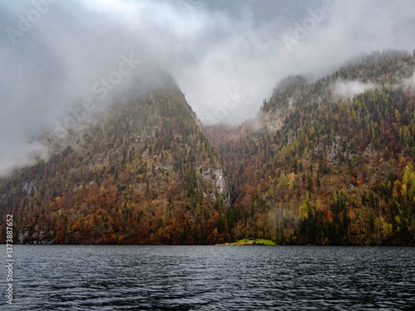 Obraz A serene lake Konigssee surrounded by misty mountains and dense autumn foliage.