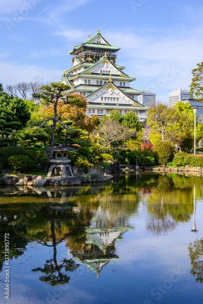 Fototapeta Osaka Castle, rebuilt in 16th century, reflects in a serene pond. Surrounding autumn foliage adds vibrant colors to this iconic Japanese landmark's splendor.