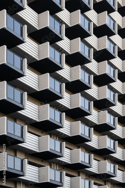 Fototapeta A modern apartment building in Osaka, Japan showcases a repeating pattern of balconies. The geometric design, with its contrasting colors and clean lines, exemplifies contemporary Asian architecture.