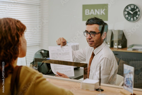 Fototapeta Businessman in professional attire sitting in bank office discussing documents with customer at bank, office environment with visible bank sign and clock in background