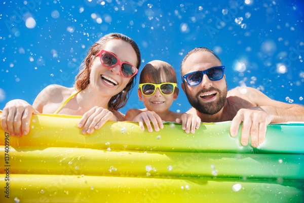 Fototapeta Happy family playing in waterpark. People having fun on summer vacation. Family jumping into swimming pool with splashes of water.