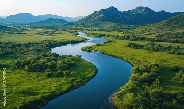 Fototapeta Scenic river winding through lush green landscape with mountains in background
