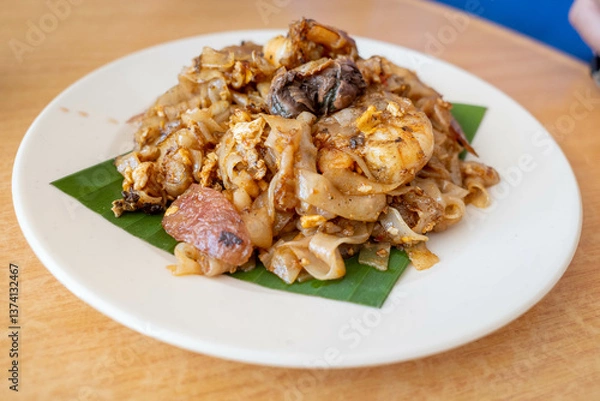 Fototapeta A plate of char koay teow or stir fried flat rice noodle dish made popular in Penang Malaysia. It is smoky flavor, sweet and savory with prawns, cockles and sausages.
