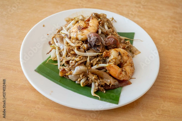 Fototapeta A plate of char koay teow or stir fried flat rice noodle dish made popular in Penang Malaysia. It is smoky flavor, sweet and savory with prawns, cockles and sausages.