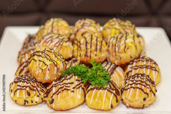 Obraz The plate showcases cream puffs drizzled with chocolate and white icing, garnished with parsley. Perfectly arranged, the dessert looks irresistibly appetizing, ideal for food lovers