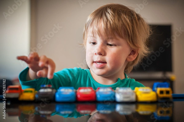 Fototapeta A young child is engaged in play with a lineup of colorful toy cars, displaying concentration and joy in a bright indoor setting during the afternoon