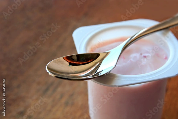 Fototapeta Strawberry pink yogurt in white plastic cup on a wooden rustic background with spoon on it with copy space.