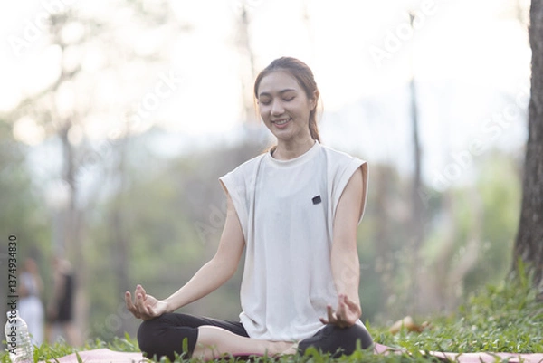 Obraz A enthusiastic Asian sports woman stopped after exercising at the garden, sitting on a exercise mat, inhaling deeply by closing her eyes. Sports and exercise regularly Health and health