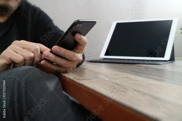 Fototapeta businessman hand using smart phone,mobile payments online shopping,omni channel,digital tablet docking keyboard computer in modern office on wooden desk