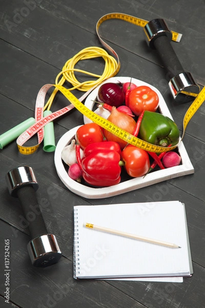 Obraz Sport and diet. Healthy lifestyle. Vegetables, dumbbells  notebook. Peppers, tomatoes, garlic, onion  radish in a heart on  black background