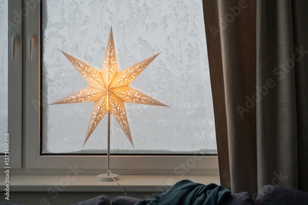 Fototapeta Illuminated electric Christmas star sits on windowsill, with snowstorm outside covering window in thick snow, creating cozy winter atmosphere