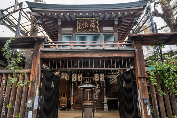 Fototapeta A weathered wooden shrine gate in Osaka, Japan. Lanterns hang, a statue stands, showing traditional Asian architecture and religious elements.
