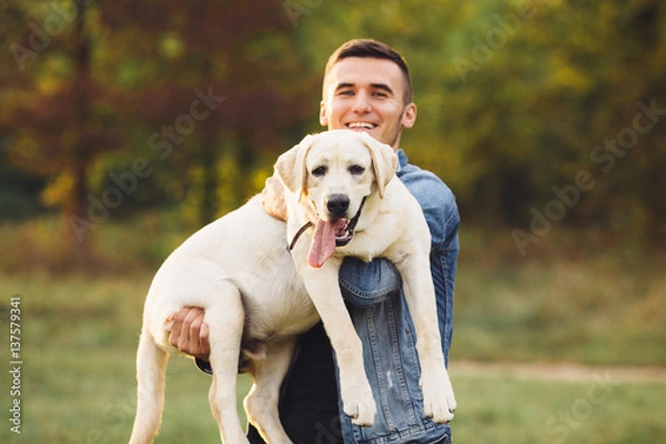 Fototapeta Portrait of happy man holding dog Labrador in hands in park