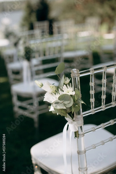 Obraz Clear chairs with white floral arrangements line a green lawn in an outdoor event setting