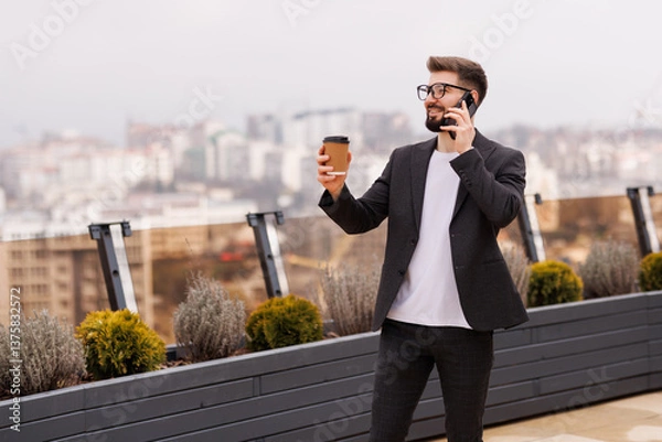 Fototapeta Take a pause. Portrait of smiling businessman drinking coffee on office balcony after talking by phone.