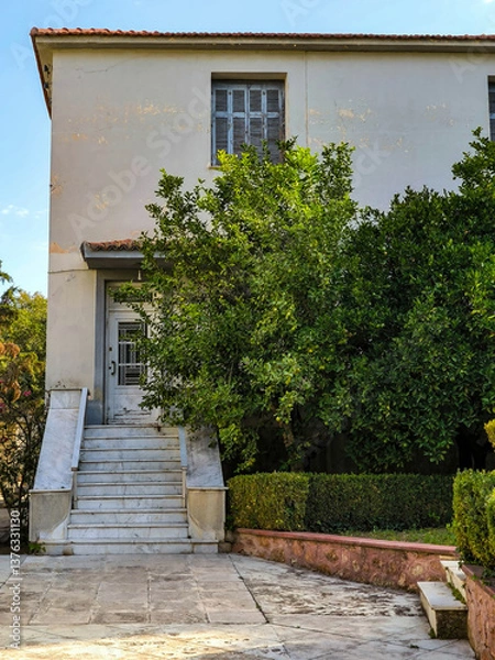 Obraz Partial front view of a classic design family house with steps to the door and green trees garden. Travel to Athens, Greece.