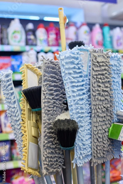 Obraz Various cleaning tools, including mops and brushes, are organized and displayed in a store aisle. The focus is on colorful microfiber mop heads and their textures.