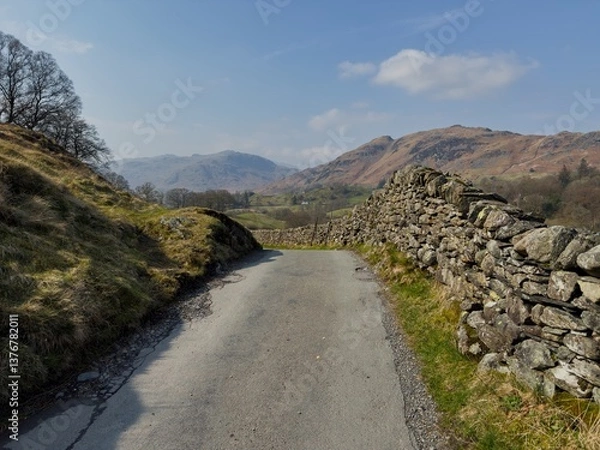 Fototapeta Narrow country lane bordered by dry stone walls with views of distant Lake District hills in spring