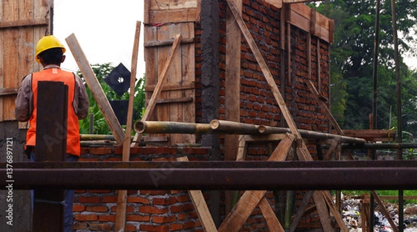 Obraz Cianjur, Indonesia - March 19, 2025: Construction Workers Building a Brick Structure with Wooden Supports Outdoors
