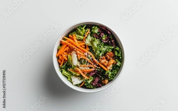 Fototapeta Overhead view of a fresh salad in a white bowl. The salad contains shredded carrots, lettuce, and sesame seeds. The background is white