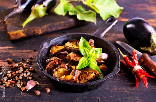 Obraz Fried eggplant in a pan. Cooking fried eggplant. Culinary tools, wooden board, knife, fork and spice