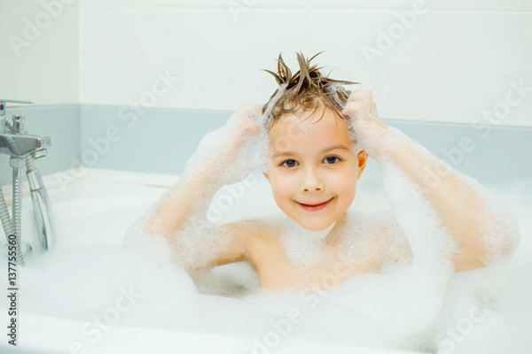 Fototapeta Happy young boy taking a bath in the foam.. Smiling child washes his head with shampoo.