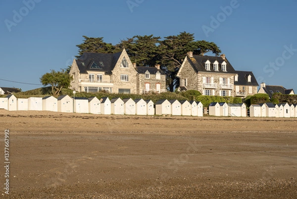 Obraz A beach at low tide with wet sand that reflects the buildings with traditional architecture  A row of beach huts typical of seaside resorts at Saint-Cast-Le-Guildo in Brittany, France