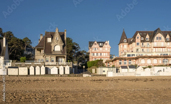 Obraz A beach at low tide with wet sand that reflects the buildings with traditional architecture  A row of beach huts typical of seaside resorts at Saint-Cast-Le-Guildo in Brittany, France