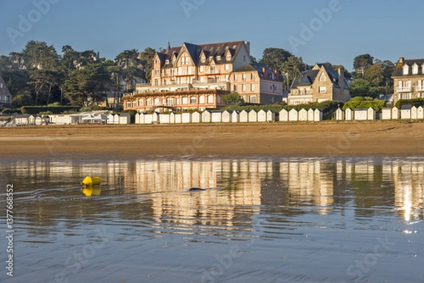 Obraz A beach at low tide with wet sand that reflects the buildings with traditional architecture  A row of beach huts typical of seaside resorts at Saint-Cast-Le-Guildo in Brittany, France