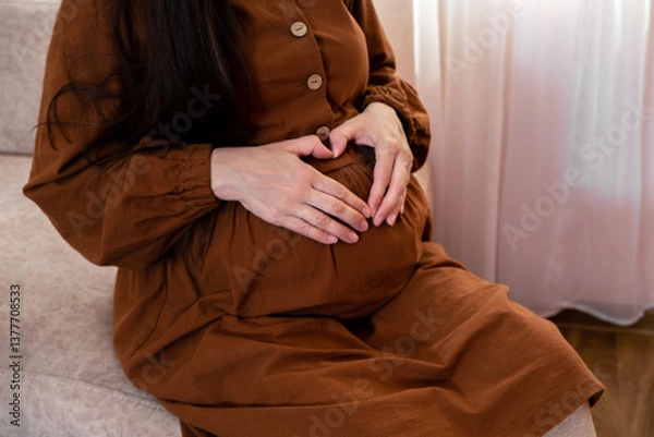 Fototapeta Pregnant woman holding palms in heart shape on her big tummy, cropped.