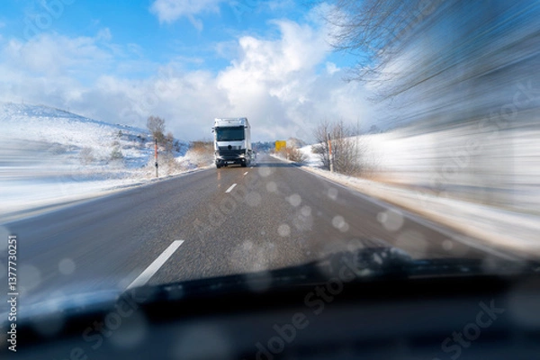 Fototapeta Heavy truck with trailer driving fast on wintry icy country roads, with poor visibility through the windscreen of a car.