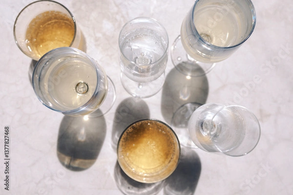 Fototapeta Glasses with various chilled alcoholic beverages on the marble table. Top view. Mineral water and champagne. Fragrant sparkling wines in bright sunlight. Copy space