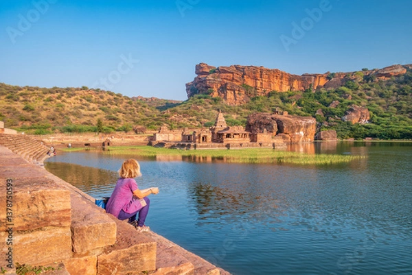 Fototapeta Woman exploring ancient ruins at Badami. Tourist sitting on lake shore relaxing at Badami temple, Karnataka, India