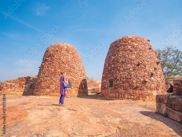 Fototapeta Woman exploring ancient temple site at Badami. Tourist walking among ruins stone walls gateways in Karnataka, India