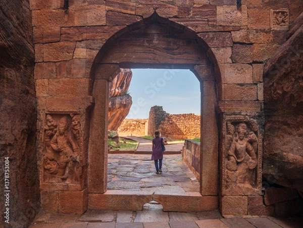 Fototapeta Woman exploring ancient temple site at Badami. Tourist walking among ruins stone walls gateways in Karnataka, India