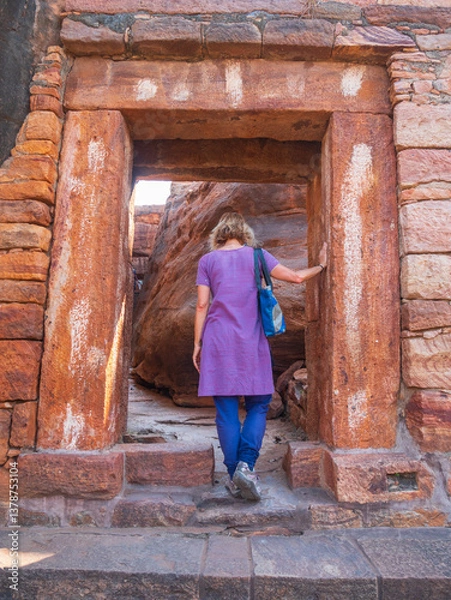 Fototapeta Woman exploring ancient temple site at Badami. Tourist walking among ruins stone walls gateways in Karnataka, India