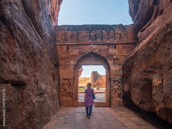 Fototapeta Woman exploring ancient temple site at Badami. Tourist walking among ruins stone walls gateways in Karnataka, India