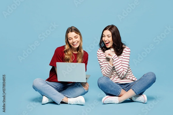 Fototapeta Full body young surprised couple two IT friends women wear red casual clothes together sit hold use work on laptop pc computer isolated on pastel plain light blue cyan background. Lifestyle concept