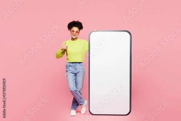 Fototapeta Full body young woman she wear green sweater casual clothes big huge blank screen mobile cell phone smartphone with workspace area show thumb up isolated on plain pink background. Lifestyle concept.