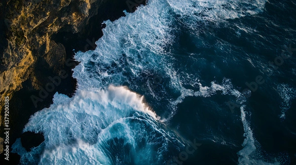 Fototapeta Aerial Top-Down View of Ocean Waves Crashing Against Rugged Cliffs with Dramatic Contrast