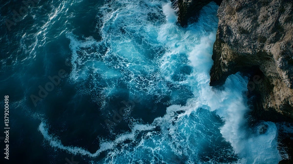 Fototapeta Aerial Top-Down View of Ocean Waves Crashing Against Rugged Cliffs with Dramatic Contrast