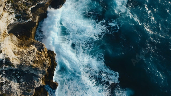 Fototapeta Aerial Top-Down View of Ocean Waves Crashing Against Rugged Cliffs with Dramatic Contrast